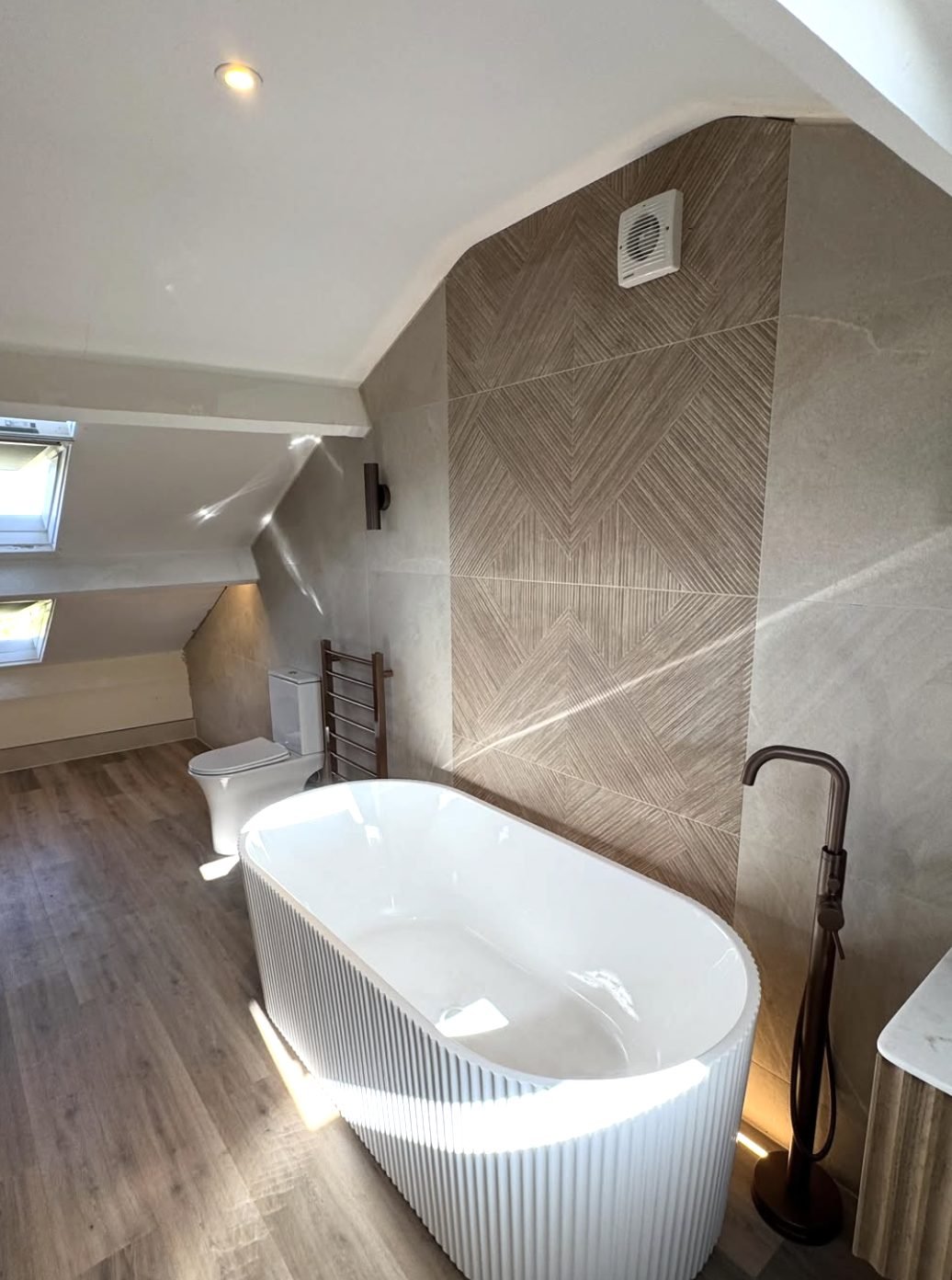 Attic bathroom with a fluted freestanding bath and bronze floor standing tap under sloping ceilings